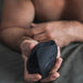 A close-up image of a man holding a Hot Octopuss Pulse Solo Essential Oscillating Penis Masturbator with buttons, focusing on his hands and the device against a blurred background.