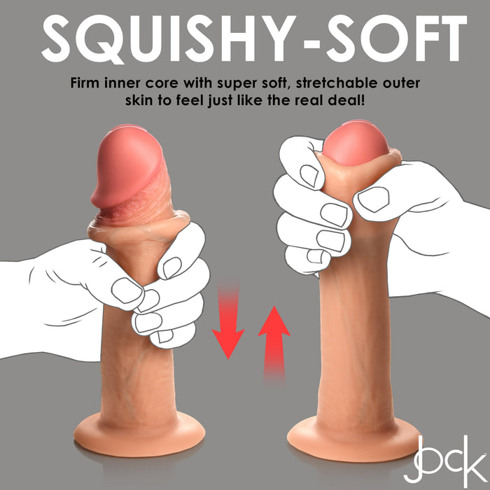 Image showing the Jock Real Skin 8 Inch Silicone Suction Cup Dildo - Vanilla by XR Brands, a realistic toy with dual density that features a firm inner core and an incredibly soft, stretchable outer skin. The toy is depicted with a hand squeezing it to demonstrate its flexibility and lifelike texture. "Squishy-Soft" is prominently displayed at the top.