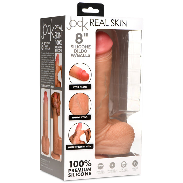 A package featuring the Jock Real Skin 8 Inch Silicone Suction Cup Dildo with Balls in Vanilla from XR Brands. The box emphasizes its realistic design with vivid glans, lifelike veins, dual-density construction, and super stretchy skin. It also highlights its strong suction cup and 100% premium silicone material.