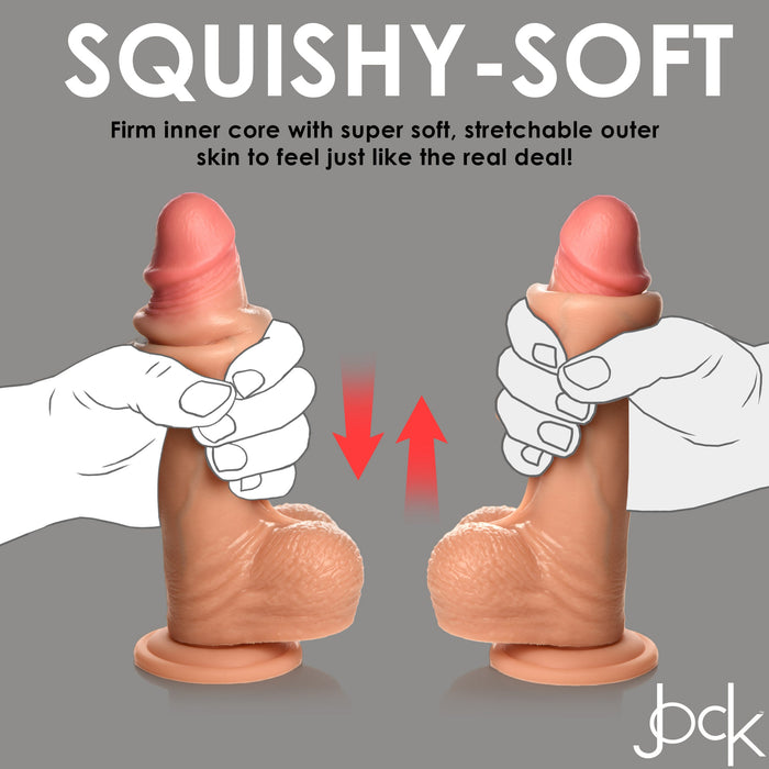 Two hands hold the Jock Real Skin 8 Inch Silicone Suction Cup Dildo with Balls - Vanilla by XR Brands, showcasing its flesh-toned, realistic erect penis shape. The toy boasts a firm inner core and a soft, stretchy outer layer for dual density pleasure. A suction cup base ensures hands-free fun. Background text highlights "Squishy-Soft" features detailing its core and skin texture.