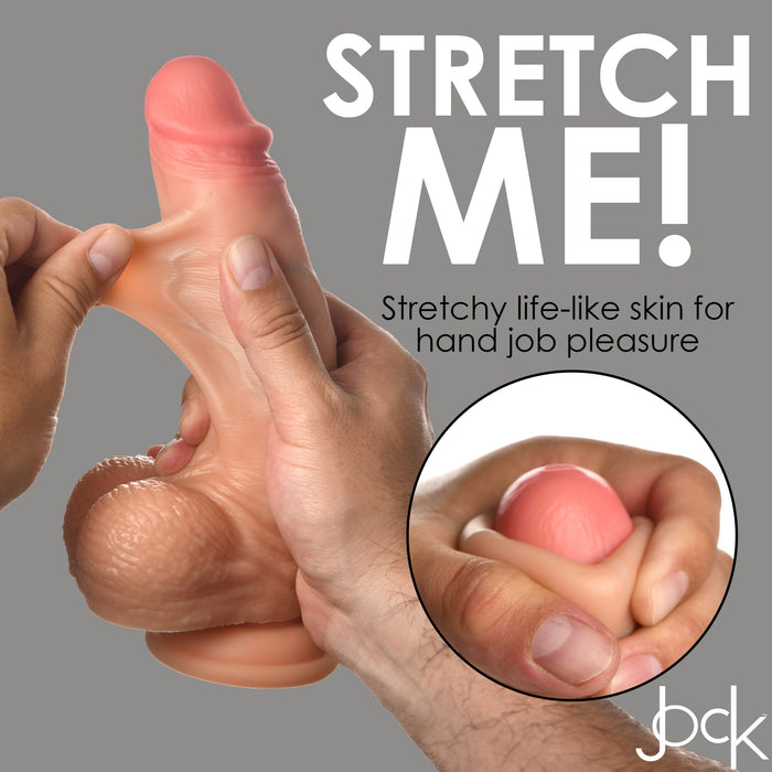 A lifelike dildo crafted from stretchy, realistic material is being held and stretched by two hands. The accompanying text says, "STRETCH ME! Stretchy life-like skin for hand job pleasure." Featuring a robust suction cup for versatile use, the caption includes the logo "buck" in the bottom right corner. Product: Jock Real Skin 8 Inch Silicone Suction Cup Dildo with Balls - Vanilla by XR Brands.