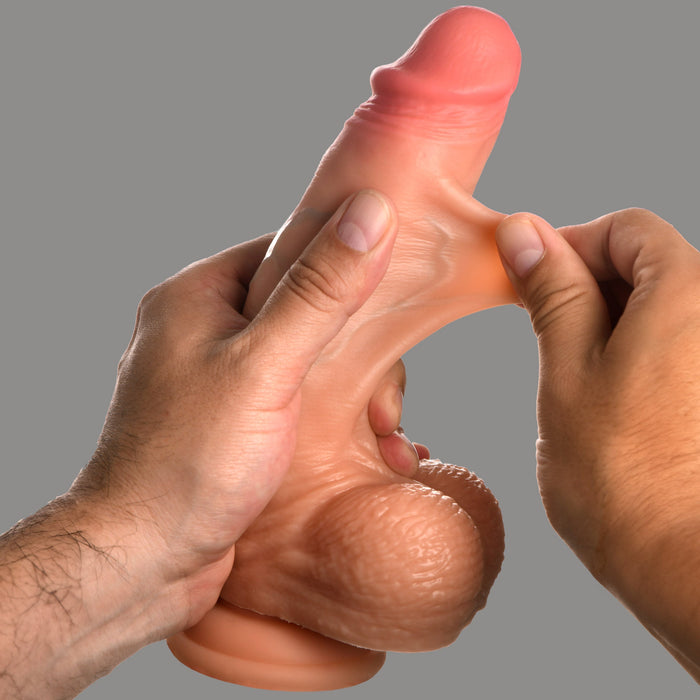 A person holds the Jock Real Skin 8 Inch Silicone Suction Cup Dildo with Balls - Vanilla by XR Brands, designed to resemble a human penis, stretching the material to demonstrate its flexibility. The background is plain and gray.