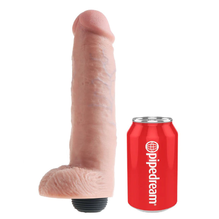 A realistic, vanilla-colored King Cock Squirting 10 Inch Dildo with Balls from Pipedream Products, featuring a textured surface and a rounded tip, stands beside a red soda can labeled "Pipedream" for size comparison. The base of this phthalate-free dildo includes a black cap or dial.