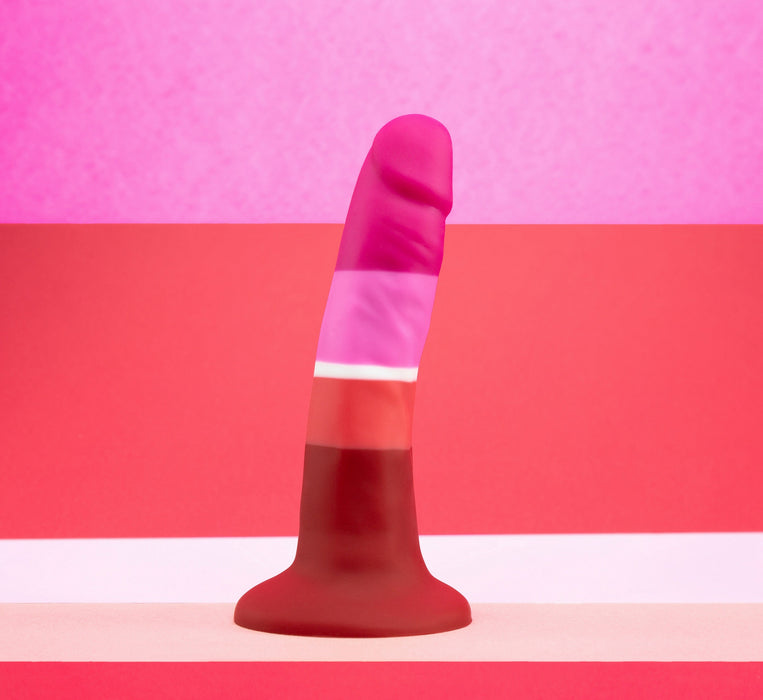 The Lesbian Pride 5.5 Inch Silicone Suction Cup Dildo by Blush showcases a stunning gradient color scheme from dark red at the base to bright pink at the tip, capturing the essence of a lesbian flag. It features alternating horizontal stripes of light and dark pink in the background, making it ideal for beginner play with its silky silicone texture.