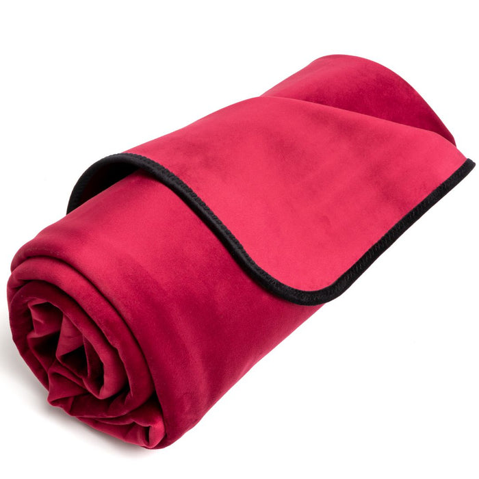 A rolled-up burgundy Liberator Fascinator Throw Mini Sized Velvety Sex Blanket with black trim on a white background.