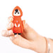 A hand holds a small figurine modeled as the Little Red First Time Discreet Powerful Bullet Vibrator by Natalie’s Toy Box. This red-caped, hooded character has black hair, a white face, and a heart symbol on its chest, complemented by black shoes. Designed to blend seamlessly into any setting, it is set against a plain white background.