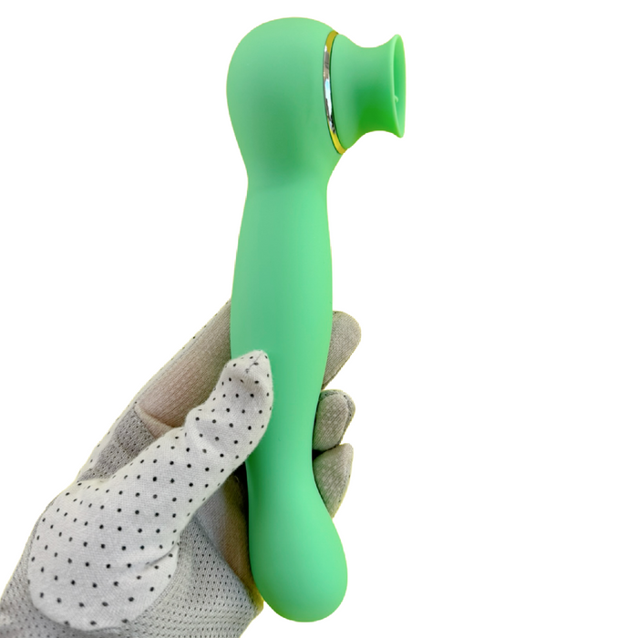 A gloved hand holding the Luscious Licker Double Ended Licking & G-Spot Vibrator in mint green, featuring a narrow, curved handle and a suction cup-like attachment at the top. The white glove with black dots on the fingers and palm perfectly complements the silky silicone texture of this Nasstoys product.