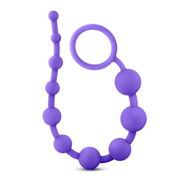 The Luxe Beginner Ultra Slim Silicone Anal Beads by Blush are body-safe and available in various colors, featuring a strand of purple silicone anal beads with bulbs of varying sizes and a retrieval ring at one end for easy handling.