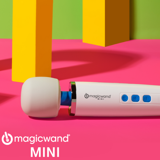 A white Magic Wand Mini Cordless Rechargeable Vibrator by Vibratex with a blue control panel is displayed on a vibrant pink surface. The massager head is on the left side, and geometric yellow and orange shapes stand in the background. The brand logo and name "Magic Wand Mini" are printed in white text, highlighting its sleek rechargeable form.