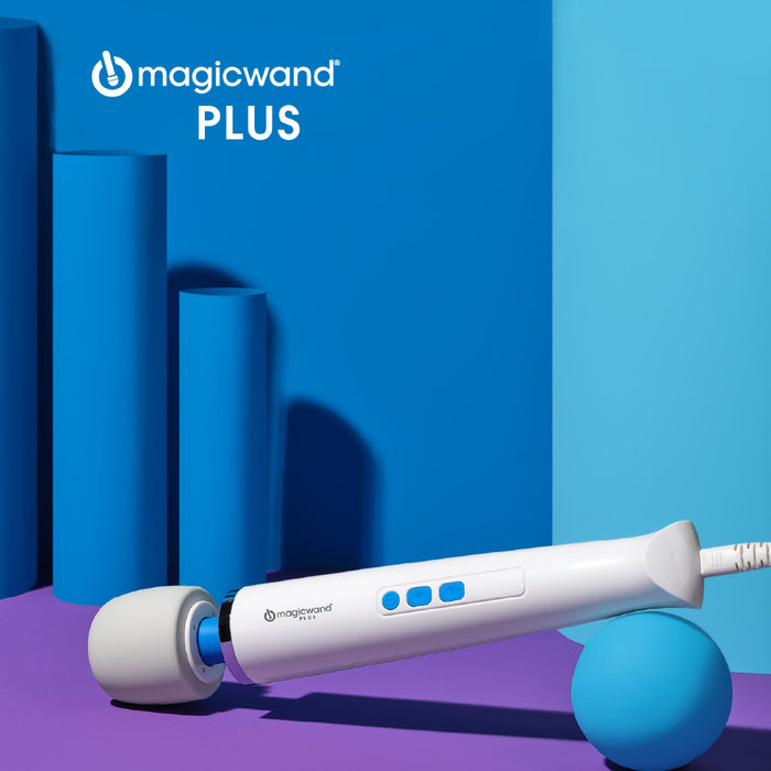 A white "Magic Wand Plus 4 Speed Ultra Powerful Wand Vibrator" by Vibratex, featuring blue buttons, rests on a purple surface, angled at the corner where blue and purple walls meet. Renowned for its deep vibrations and variable speeds, the vibrator is positioned next to a blue sphere with cylindrical blue shapes in the background. The text "magic wand PLUS" is displayed above.