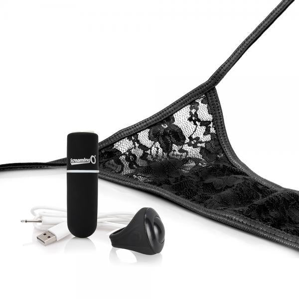 A pair of black lace panties is partially shown lying on a white surface. Next to the My Secret Remote Control One Size Vibrating Panties by Screaming O are a small cylindrical black device with a logo, a black silicone attachment, and a USB charging cable, suggesting this intimate wearable product includes waterproof features and possibly wireless remote control.