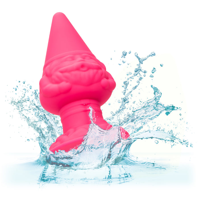 The Naughty Bits Girthy Pink Gnome Butt Plug by CalExotics, featuring a bright pink design with a pointed hat and happy expression, is partially submerged in water. Splashes and droplets are captured around the gnome against a white background, creating a dynamic and playful scene reminiscent of fulfilling playtime.