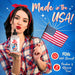 A woman with long dark hair and a red headband, dressed in a plaid shirt, holds an American flag and a bottle of Naughty Jane's Sex Sauce Natural Water Based Lubricant 8oz from XR Brands, labeled "Made in the USA." The text highlights FDA clearance and paraben & glycerin-free features. A blue background adorned with stars completes the image.