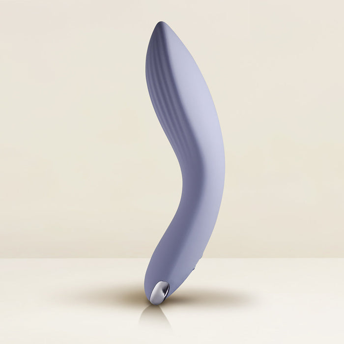 A sleek, curved, lavender-colored Niya N2 Powerful Textured Solo and Couples Vibrator by Rocks Off stands upright against a neutral background. The design is ergonomic, featuring smooth lines and subtle ridges on one end, complemented by a powerful motor with 10 modes of vibrating function for broad stimulation.