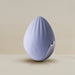 A palm-held device from Rocks Off, the Niya N4 Palm Held Powerful Textured Egg Vibrator, is egg-shaped and light purple with a smooth texture and a ripple pattern on top. It features a teardrop logo with an embedded wireless symbol. Made of silky silicone, this vibrator offers a powerful 10-function motor and rests on a shiny, curved metallic stand against a neutral beige background.