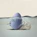 An egg-shaped, light purple waterproof device partially submerged in water, with air bubbles rising to the surface. It sits on a small piece of coral. The silicone Niya N4 Palm Held Powerful Textured Egg Vibrator by Rocks Off features a 10 function motor. The background is neutral, emphasizing the aquatic theme.