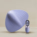 The Niya N5 Flexible Lay On Humping Vibrator with Remote by Rocks Off, showcased in a light lavender shade with a shell-like design and textured surface, is displayed alongside its smaller, oval-shaped remote control featuring two buttons. Both waterproof items are set against a neutral background with soft lighting.