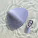 In shallow, rippling water lay the Niya N5 Flexible Lay On Humping Vibrator with Remote by Rocks Off. This smooth, translucent, shell-shaped vibrator and its sleek matching remote are waterproof and possess a soft lavender hue. Their modern design creates a serene and minimalist aesthetic.