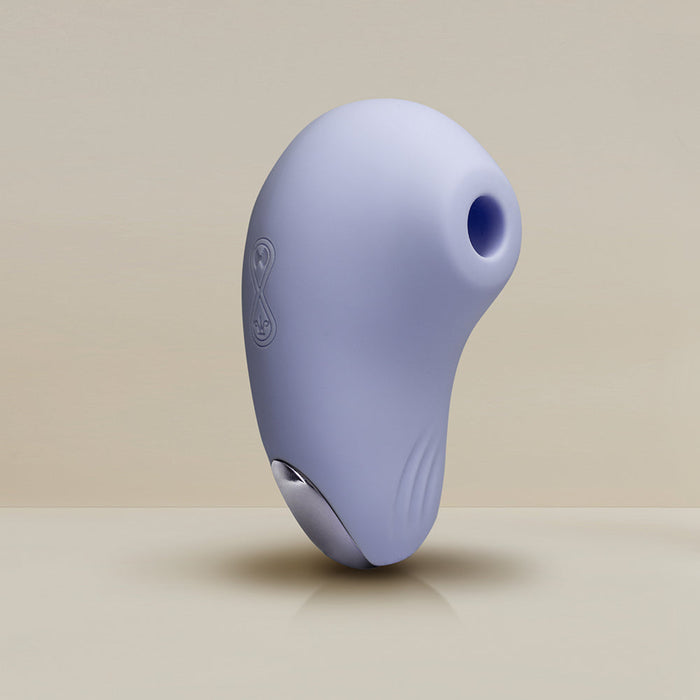 Image of the Niya N6 Ergonomic Easy Grip Clitoral Air Stimulator Vibrator by Rocks Off, a streamlined, light blue handheld device with a small circular opening at the top. The surface is smooth with a subtle, ergonomic shape and a faintly visible logo on the side. Incorporating air pulsation technology for clitoral suction, the device has metallic accents on the lower part against a plain, gradient beige background.