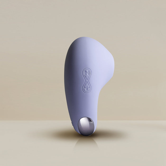 A sleek, light purple handheld device with an ergonomic design, the Niya N6 Ergonomic Easy Grip Clitoral Air Stimulator Vibrator by Rocks Off features a circular metallic component and an infinity symbol engraved on its surface. This modern marvel incorporates air pulsation technology, perfect for users seeking the ultimate experience. The soft beige background emphasizes its minimalist aesthetics.