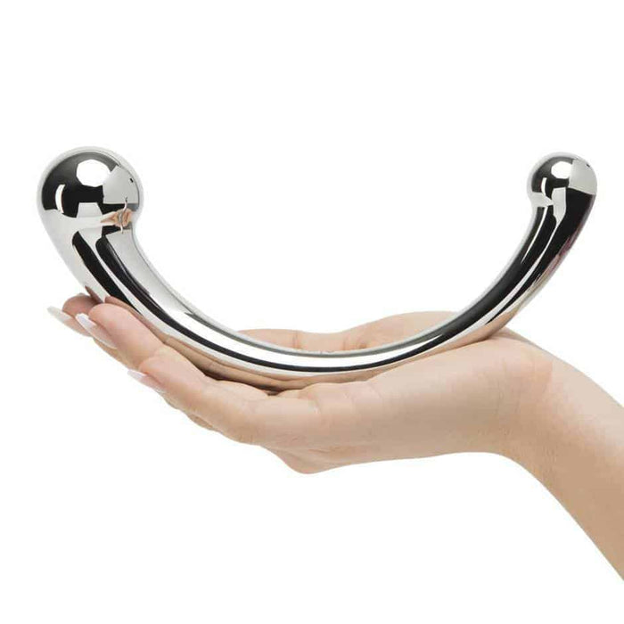 A hand holding the Njoy Pure Wand Double Ended 8 Inch Steel Dildo, a shiny, curved object made of medical-grade stainless steel with a sphere on each end. The U-shaped design is perfect for G-spot stimulation, with its non-porous surface gleaming against the plain white background.