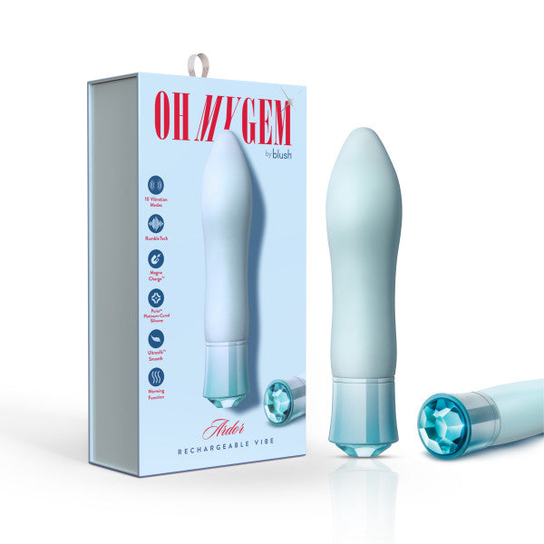 A white and light blue USB rechargeable vibrator stands next to its packaging, labeled "Oh My Gem Ardor Aquamarine Warming Internal & External Tapered Vibrator by Blush." The box features product highlights, a jeweled detail at the bottom matching the design of the vibrator, and information about its warming function.