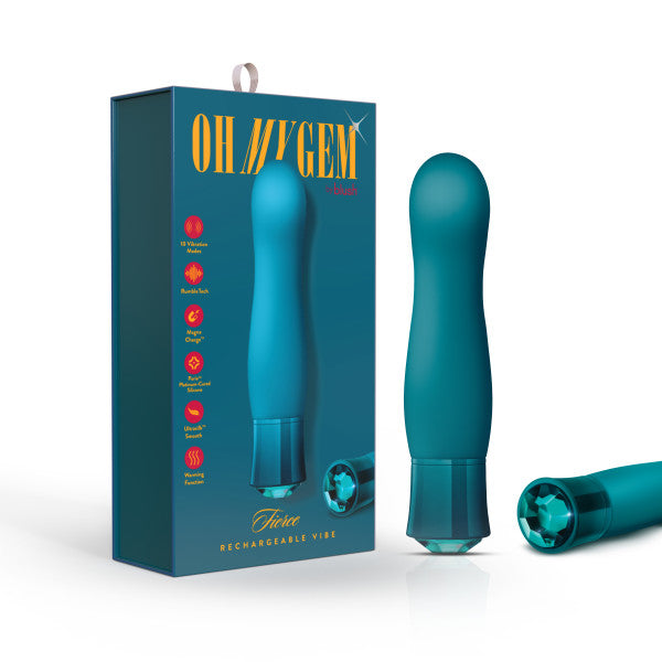 A teal-colored miniature vibe with a gem-like base is displayed next to its packaging. The packaging features the brand name "Blush" and the product name "Oh My Gem Fierce Blue Topaz Warming G-Spot Vibrator," highlighting that it has 10 vibrating functions, is rechargeable, waterproof, and made from silicone phthalate-free material.