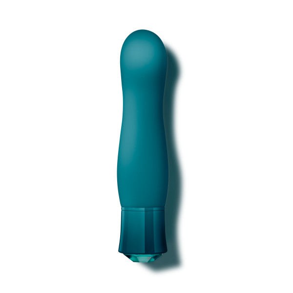 A teal-colored, cylindrical miniature vibe called the "Oh My Gem Fierce Blue Topaz Warming G-Spot Vibrator" by Blush is shown against a white background. It features a slightly curved tip and a rounded base, with the object's shadow visible on the right side. Made from silicone and phthalate-free, this vibrator offers 10 vibrating functions for ultimate pleasure.