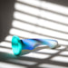 The Opal Dreams Blue Ombre 6 Inch G Spot Dildo by Blush, with its vibrant gradient transitioning from blue to green, rests on a white surface with light and shadow patterns from window blinds creating an interplay of light and shadows over the ultra-smooth silicone object.