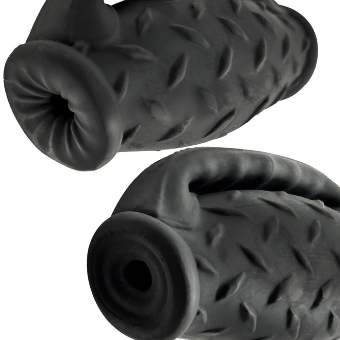 Two non-toxic Oxballs Oxballs Masterjack Double Ended Ultra Squishy Strokers with Handle - Black in the shape of tires with a handle, featuring a textured diamond plate pattern. One toy is positioned horizontally, while the other is tilted. The toys have hollow centers for stuffing treats.