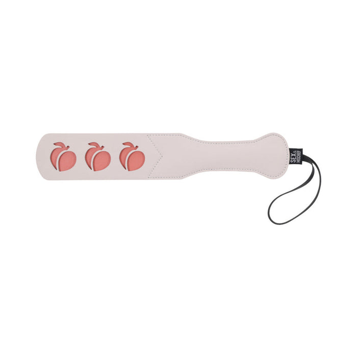 The Sportsheets Peaches 'n Cream Impression Paddle is elegantly crafted from smooth faux leather, featuring three peach-shaped cutouts and a black wrist strap, making it ideal for impact play.