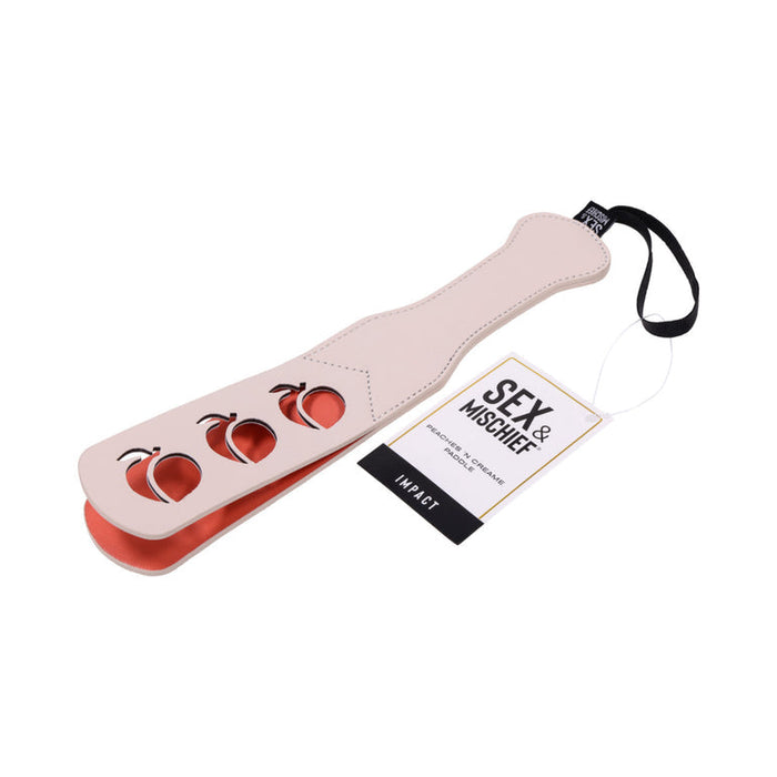 The Peaches 'n Cream Impression Paddle by Sportsheets is designed in beige and red faux leather with three apple-shaped cutouts. Perfect for impact play, it also includes a black strap at the handle end with a tag that reads "Sex & Mischief.