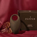 A couple's Pepper Connect Vibrating Cock Ring, presented on a luxurious maroon fabric background alongside an exotic leaf and elegant packaging.