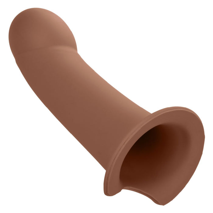 A brown knee-high boot with a CalExotics Performance Maxx Smooth Hollow Dildo Silicone Strap-on Penis Extension (Dark), laying on its side, isolated on a white background.