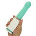 A hand holds the Pillow Talk Feisty Thrusting Vibrator with Case by BMS Enterprises, showcasing its teal and white design. The vibrator features a slightly curved, ribbed tip and a textured shaft. The handle is adorned with a diamond pattern and includes a metallic ring near the base. Made from soft, flexible material, this USB rechargeable device offers convenience and ease of use.