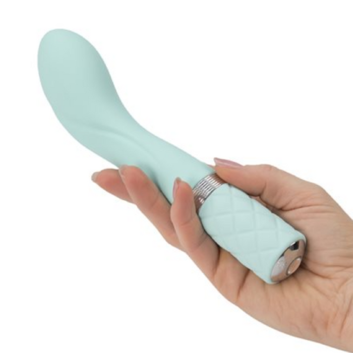 A hand holds the BMS Enterprises Pillow Talk Sassy Rumbly Rechargeable G-spot Vibrator in teal, featuring a light blue hue with a curved shape, textured handle, and metallic ring near the base. This smooth design massager appears to be made of soft material and is waterproof for versatile use.