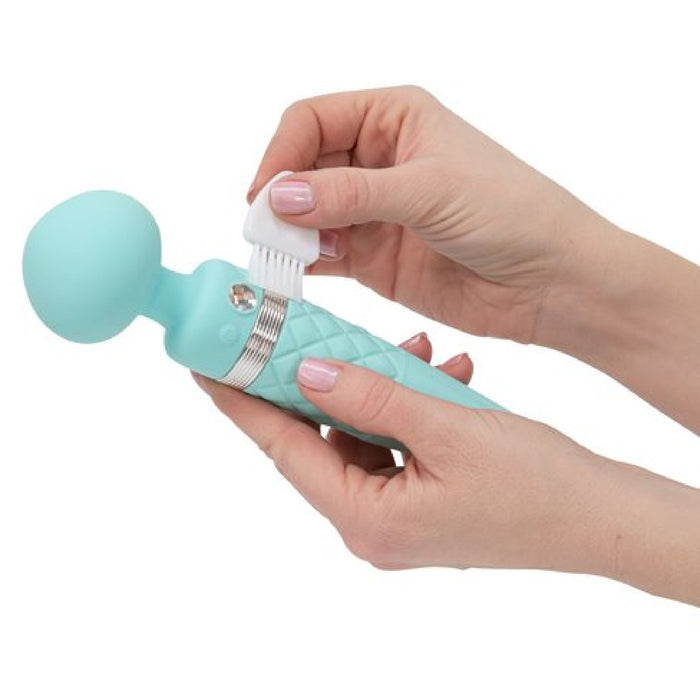 A pair of hands holds the Pillow Talk Sultry Warming Double Ended Wand Vibrator by BMS Enterprises in teal, a personal massager with a rounded head. One hand is attaching or removing a small white brush head from the premium silicone vibrator, which delivers powerful vibrations. The massager also features a silver metallic ring near its head.