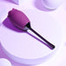 The Playboy Petal Flicking Tongue Double Ended Rose with Vibrating Stem by Evolved Novelties, a rose-shaped, purple vibrator with a sleek, black handle and silicone coating, rests on a circular white platform. The background features softly lit spheres that enhance the minimalist, modern aesthetic with purple-tinted lighting. This waterproof device ensures versatility and ease of use.