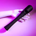 A mannequin hand holds the Playboy Royal Rechargeable Black Silicone Wand Vibrator by Evolved Novelties, featuring a sleek, black design with a textured handle and button controls, set against a vibrant purple background. This powerful wand is USB rechargeable, ensuring convenience and consistent performance.