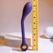 The Playboy Spot On Rechargeable Posable Silicone G-spot Vibrator by Evolved Novelties, a flexible, purple leaf-shaped massager, stands vertically beside a yellow measuring tape. The tape shows it's about 11 inches tall. Crafted from premium silicone, this poseable device is set against a white, minimalist background with circular and cylindrical shapes.