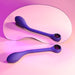 A sleek, purple *Playboy Spot On Rechargeable Posable Silicone G-spot Vibrator* by *Evolved Novelties* is placed on a pastel pink background, creating a soft and inviting aesthetic. The velvet smooth silicone toy is reflected in a curvaceous, irregularly shaped mirror, adding a dynamic visual element with a gradient lighting effect.