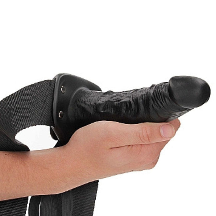 Black Realrock 6 Inch Hollow Dildo & Strap-on Harness being held by a hand on a white background