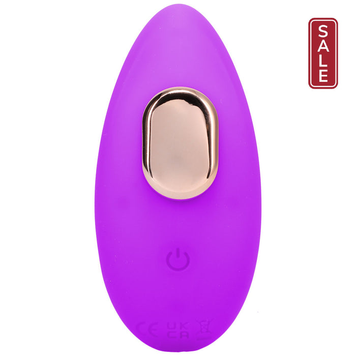 A small, oval-shaped, purple Remote Controlled Panty Vibrator for Beginners in a Bag by Doc Johnson, featuring a gold button on top and a power symbol near the bottom. The device appears to be made of a smooth, soft material and has an eco-friendly design.