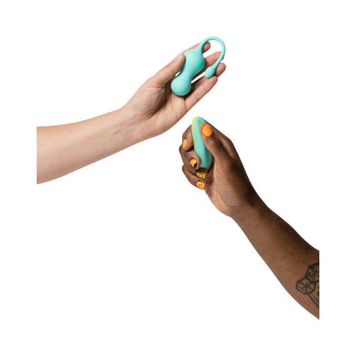 Two hands holding green sexual wellness devices against a white background. One hand, with light skin, holds the Romp Cello Remote Control Vibrating Egg from WOW, while the other hand, with dark skin and a tattoo, holds a small, rounded G-Spot Vibrator. Both premium silicone devices have yellow accents.