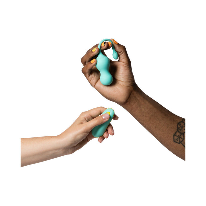 Two hands holding a turquoise Romp Cello Remote Control Vibrating Egg from WOW, made of premium silicone. The right hand, which has a cube tattoo on the wrist, is holding the vibrator, while the left hand holds the wireless remote. The background is white.