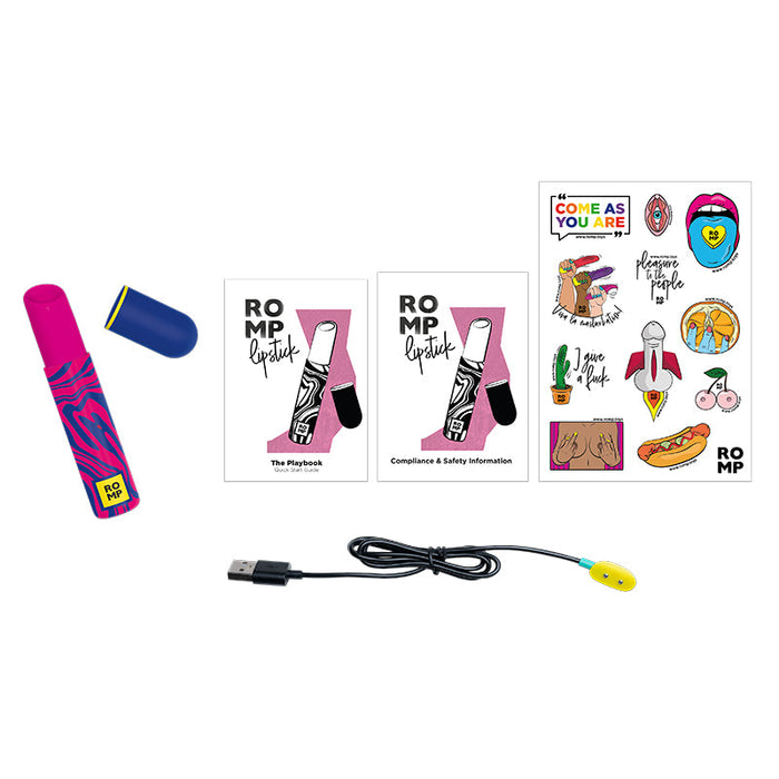 The ROMP Lipstick First Time Pleasure Air Clitoris Stimulator Vibrator by WOW, in vibrant pink and blue, rests beside its cap. It is surrounded by a playbook, a compliance and safety information booklet, playful stickers, and a USB charging cable with a yellow end. Equipped with Pleasure Air Technology, this clitoral stimulator promises delightful sensations.