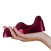 A hand is holding the Ruby Glow Blush External Grinding and G-Spot Vibrator with Remote by Rocks Off, a sleek, ergonomically designed maroon object with flowing curves. The object appears to be a stylish, contemporary piece of art featuring G-spot action and boasts a smooth, glossy finish. The background is plain white.