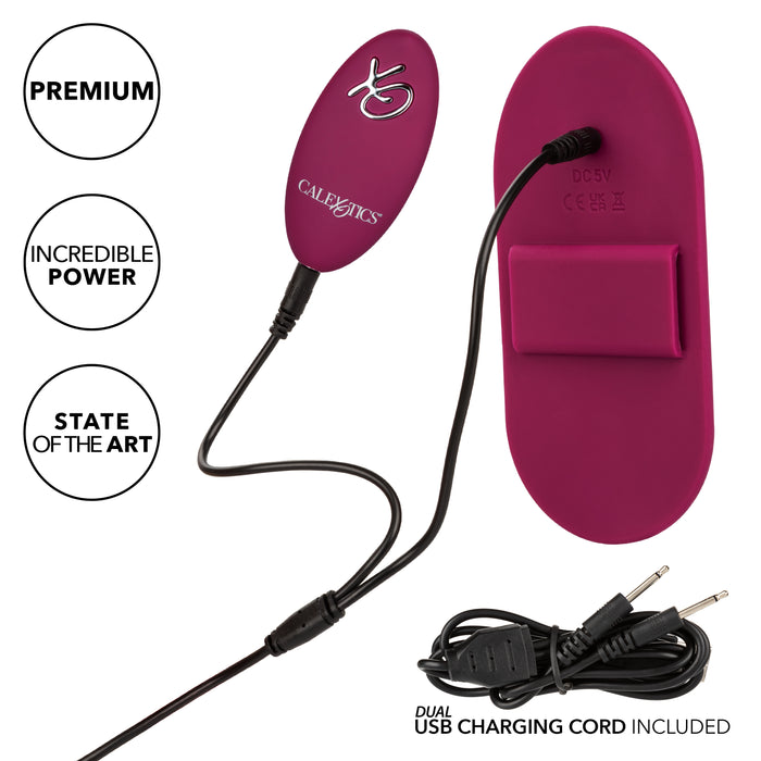 The magenta Dual Rider Strap-on Grinding Pad with Remote Control by CalExotics boasts two oval components connected by a cable, featuring text such as "Premium," "Incredible Power," and "State of the Art." Enhanced with vibrating ridges, this pad promises an unbeatable experience.