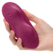 A hand holding a Dual Rider Strap-on Grinding Pad by CalExotics, featuring an Oval-shaped design in purple with textured patterns and a convenient wireless remote control.