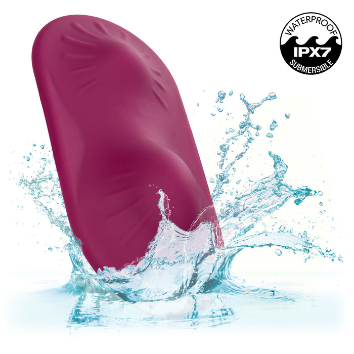 A pink, waterproof Dual Rider Strap-on Grinding Pad with vibrating ridges from CalExotics is partially submerged in splashing water. The IPX7 rating is shown, indicating it is submersible.